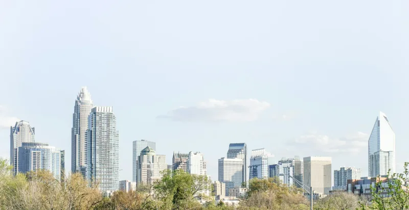 The Charlotte skyline seen across low-rise rooftops and trees on a clear day.